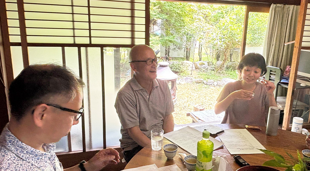 共創・連携の風景。縁側のある落ち着いた古民家風の空間で、異なる組織のメンバーが円卓を囲み、リラックスした雰囲気で対話を行いながら、パートナーシップを深めている様子